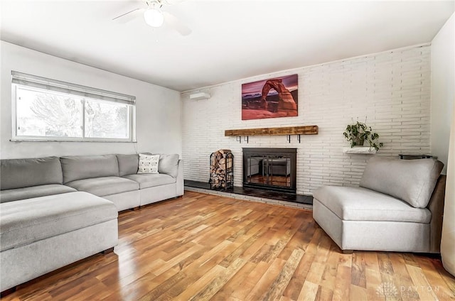 living room featuring a brick fireplace, brick wall, a ceiling fan, and wood finished floors