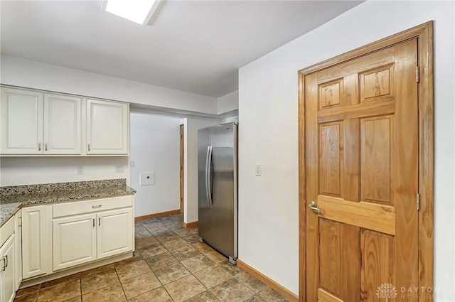 kitchen with white cabinetry, baseboards, dark stone countertops, and freestanding refrigerator