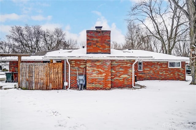 snow covered house featuring a chimney and brick siding