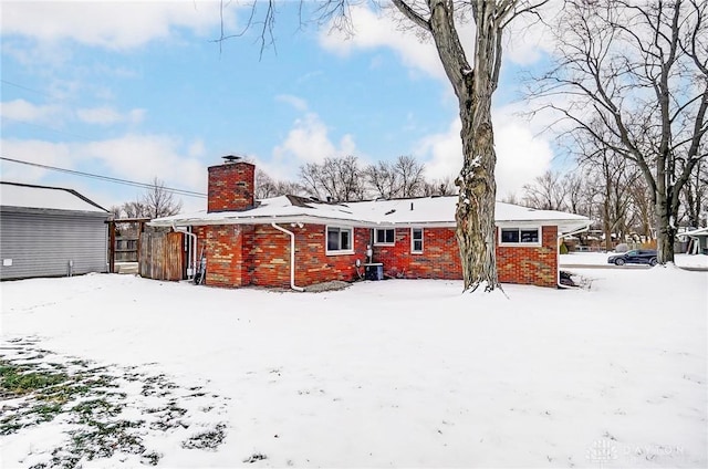 snow covered property with brick siding and a chimney