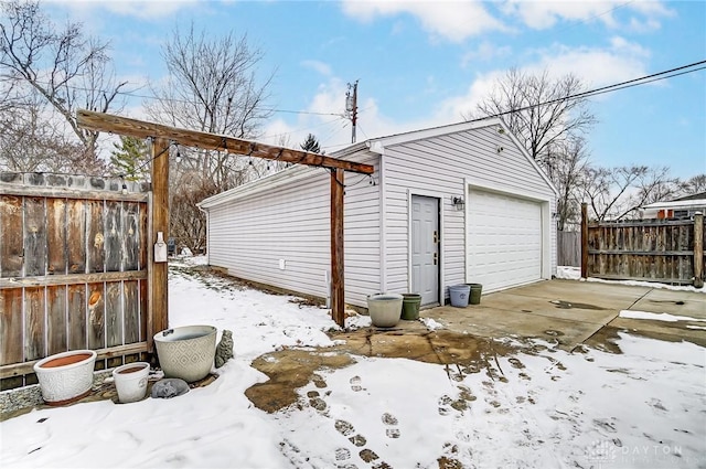 snow covered garage with a detached garage, driveway, and fence