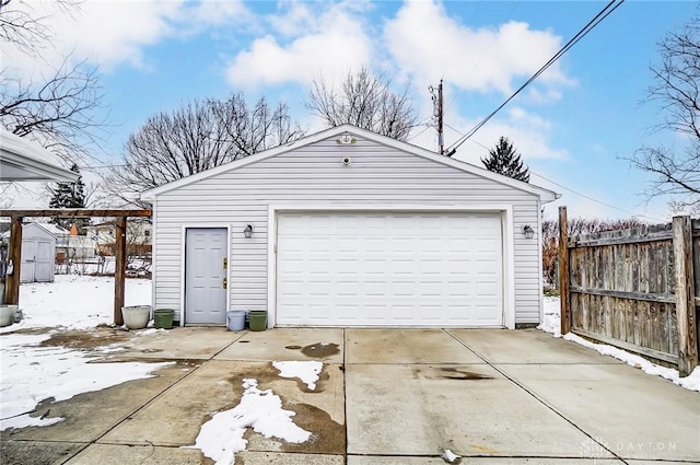 snow covered garage featuring a garage and fence