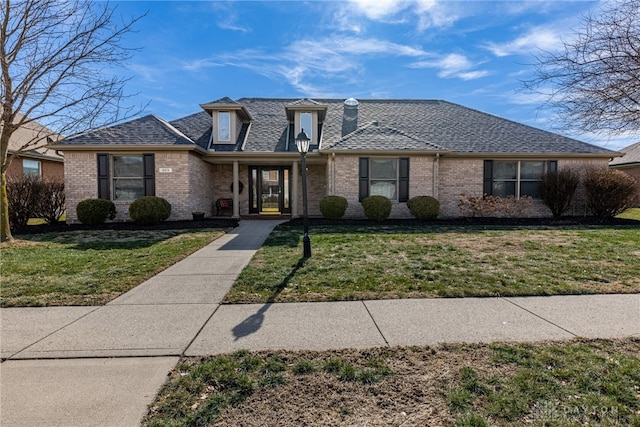 view of front of house with a front yard, brick siding, and roof with shingles