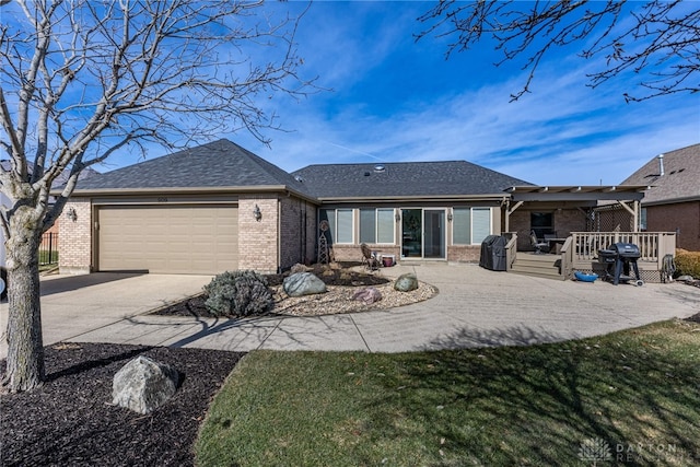 back of property with an attached garage, brick siding, a shingled roof, driveway, and a wooden deck