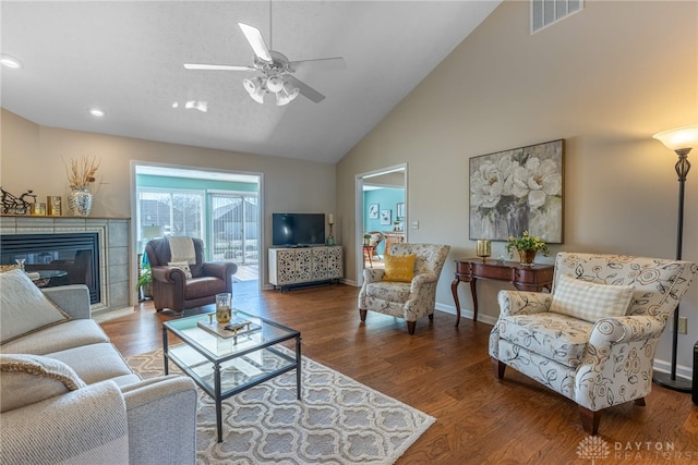 living room with baseboards, visible vents, a tiled fireplace, and wood finished floors