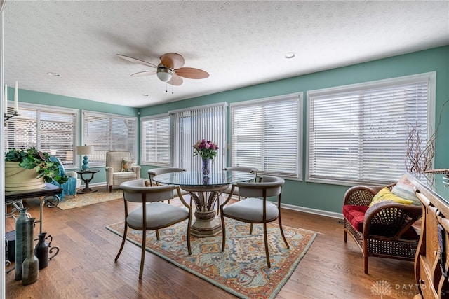 dining room with ceiling fan, a textured ceiling, baseboards, and wood finished floors