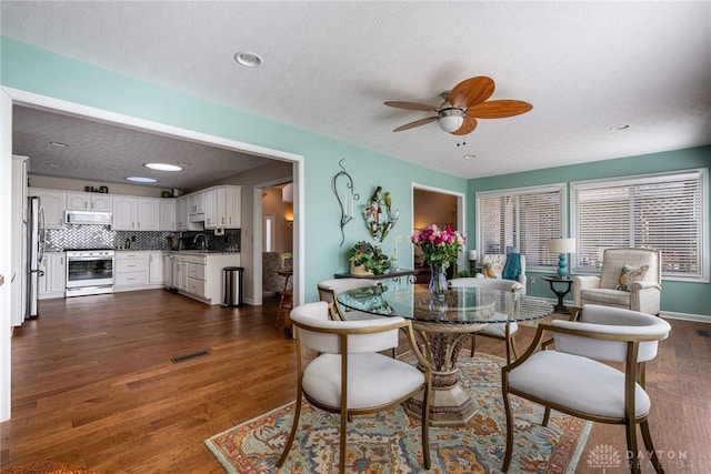 dining room featuring a textured ceiling, visible vents, baseboards, a ceiling fan, and dark wood-style floors