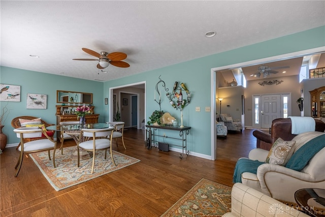 living area with ceiling fan, a textured ceiling, baseboards, and dark wood-style flooring