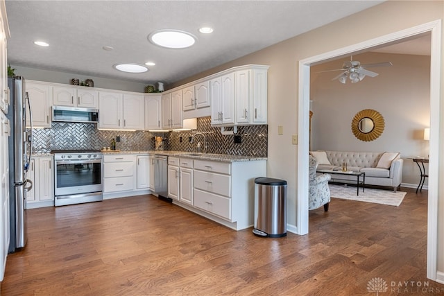 kitchen featuring appliances with stainless steel finishes, open floor plan, white cabinetry, a sink, and wood finished floors