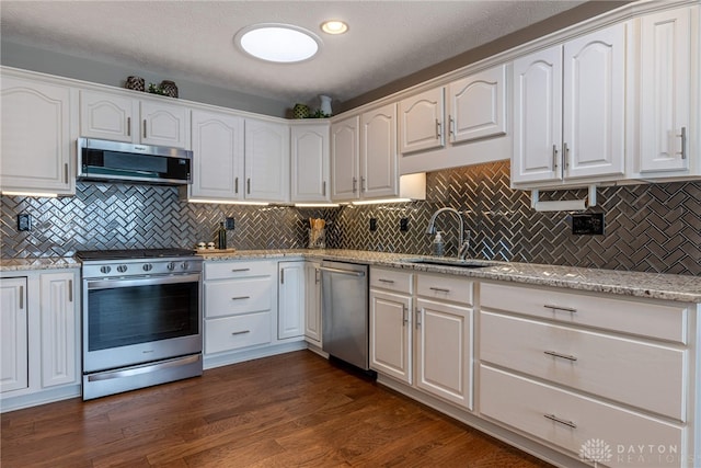 kitchen featuring dark wood-style floors, appliances with stainless steel finishes, white cabinetry, a sink, and light stone countertops