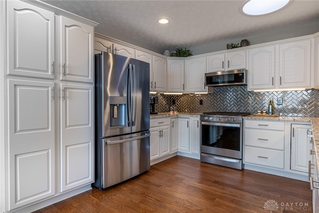 kitchen with appliances with stainless steel finishes, white cabinets, dark wood-type flooring, and light stone countertops