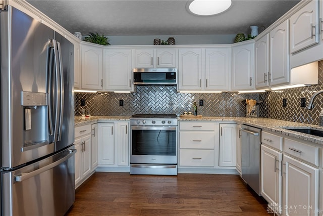 kitchen with appliances with stainless steel finishes, dark wood finished floors, light stone counters, and white cabinetry