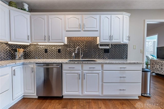 kitchen featuring light stone counters, a sink, white cabinetry, stainless steel dishwasher, and dark wood finished floors