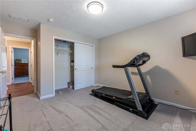 exercise area featuring light colored carpet, visible vents, a textured ceiling, and baseboards