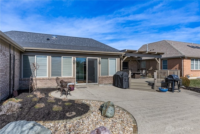 rear view of property with brick siding, a patio, a shingled roof, a pergola, and a wooden deck