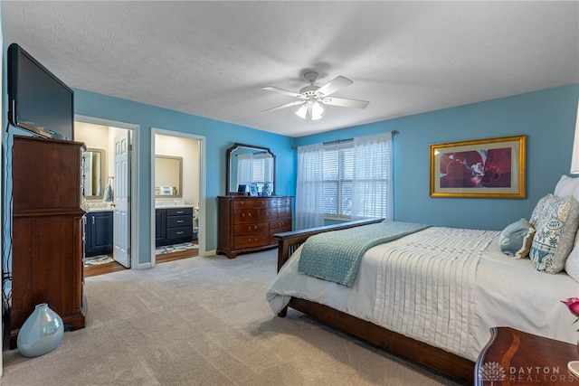 bedroom featuring ensuite bathroom, a ceiling fan, light carpet, a textured ceiling, and baseboards