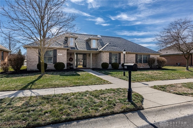 view of front of home with brick siding, a front lawn, and roof with shingles