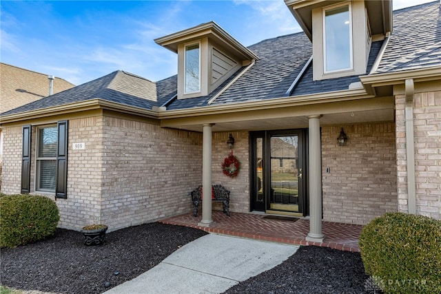 view of exterior entry with brick siding, a porch, and a shingled roof