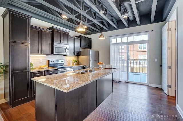 kitchen with a center island with sink, decorative backsplash, appliances with stainless steel finishes, light stone countertops, and a sink