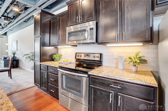 kitchen with dark brown cabinetry, tasteful backsplash, appliances with stainless steel finishes, light stone countertops, and light wood-type flooring