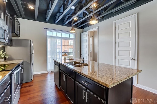 kitchen featuring light stone counters, a sink, appliances with stainless steel finishes, a center island with sink, and pendant lighting