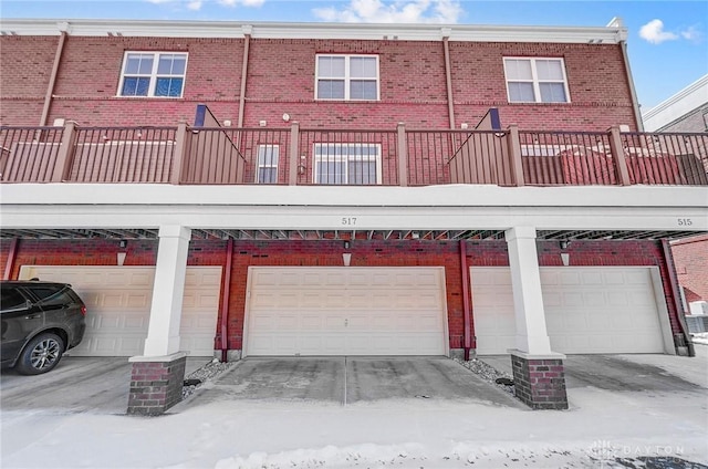 snow covered property featuring an attached garage and brick siding