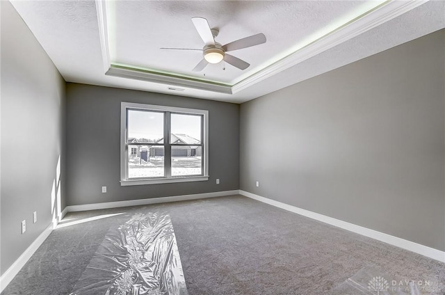 unfurnished room featuring a tray ceiling, baseboards, and carpet