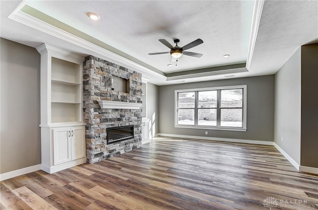 unfurnished living room featuring a raised ceiling, ornamental molding, a ceiling fan, and a stone fireplace