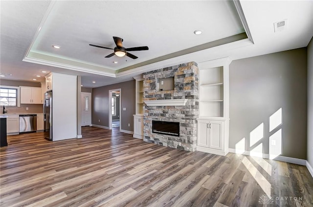 unfurnished living room featuring wood finished floors, baseboards, a ceiling fan, and a raised ceiling