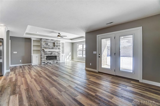 unfurnished living room featuring a tray ceiling, wood finished floors, ceiling fan, and baseboards