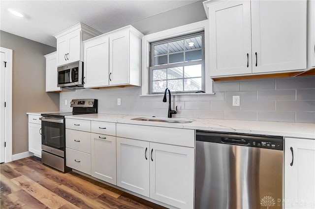 kitchen with tasteful backsplash, white cabinetry, appliances with stainless steel finishes, wood finished floors, and a sink