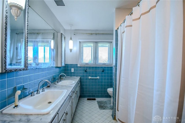 bathroom with double vanity, tile walls, visible vents, and a sink