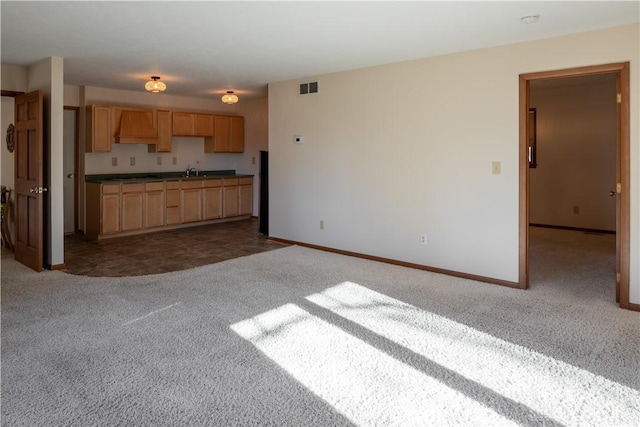 kitchen with visible vents, dark carpet, light brown cabinets, a sink, and baseboards