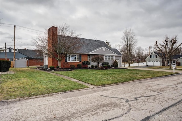 view of front facade with a front yard, cooling unit, roof with shingles, a chimney, and brick siding