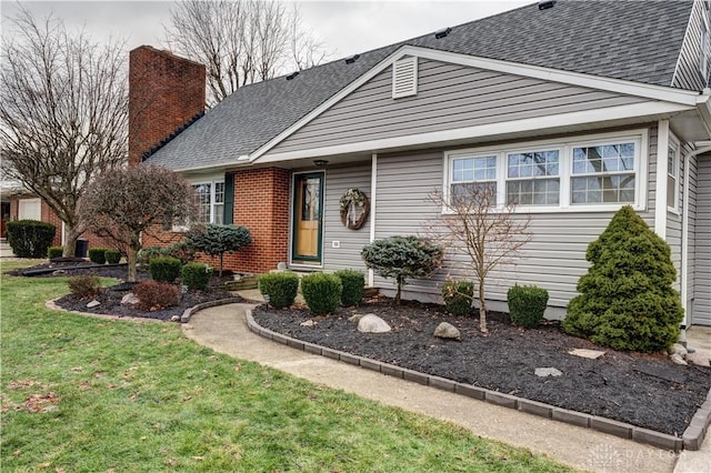 view of front of home featuring a front yard, brick siding, a chimney, and a shingled roof