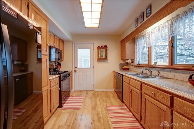 kitchen with light wood finished floors, light countertops, brown cabinets, black appliances, and a sink