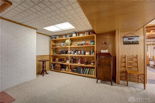 sitting room with carpet, brick wall, crown molding, and wood walls