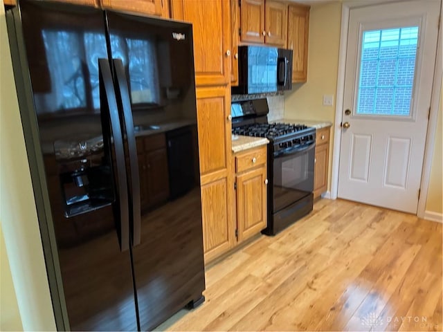 kitchen featuring brown cabinetry, light wood-style flooring, black appliances, and light countertops