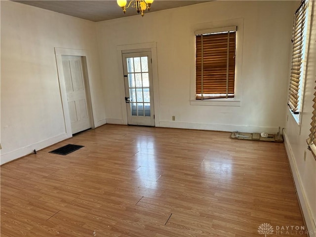 empty room featuring light wood-style floors, a chandelier, visible vents, and baseboards