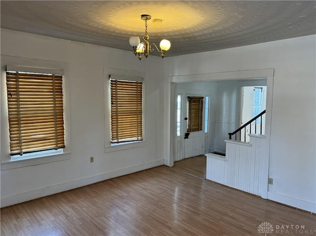 spare room with a chandelier, stairs, baseboards, and wood finished floors