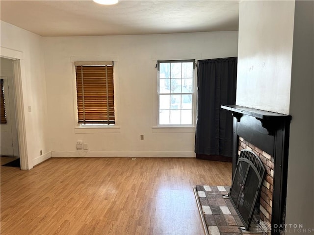 unfurnished living room with a brick fireplace, light wood-style flooring, and baseboards