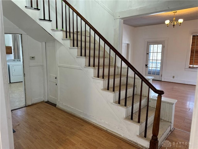 staircase with washer / dryer, a notable chandelier, and wood finished floors