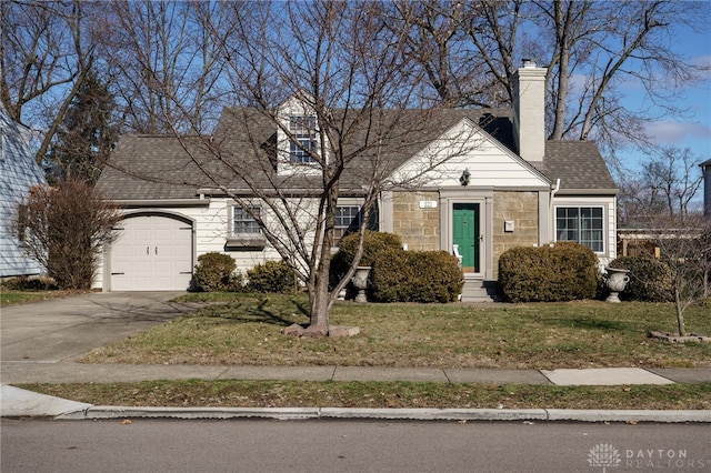 cape cod house featuring a shingled roof, concrete driveway, stone siding, an attached garage, and a front lawn