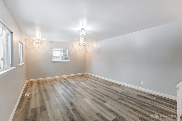 empty room with wood finished floors, visible vents, and baseboards