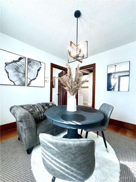 dining room featuring baseboards, a textured ceiling, wood finished floors, and a notable chandelier