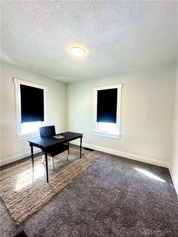 home office featuring baseboards, dark colored carpet, and a textured ceiling