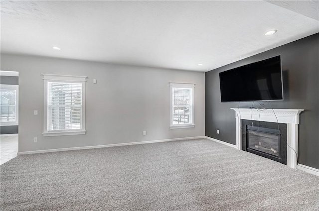 unfurnished living room featuring baseboards, a healthy amount of sunlight, a glass covered fireplace, and light colored carpet