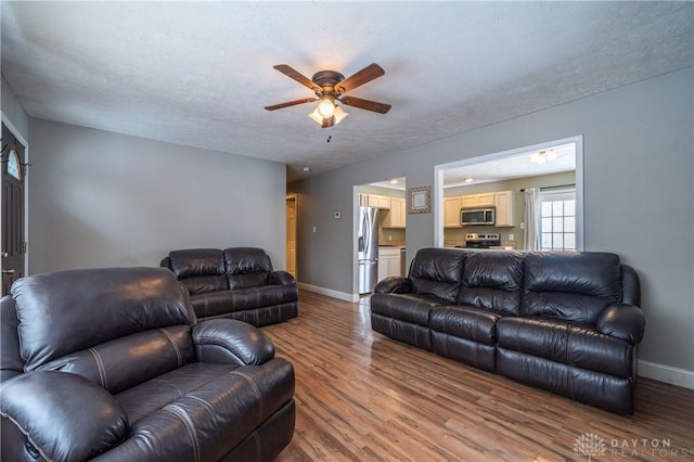 living room with a ceiling fan, a textured ceiling, baseboards, and wood finished floors