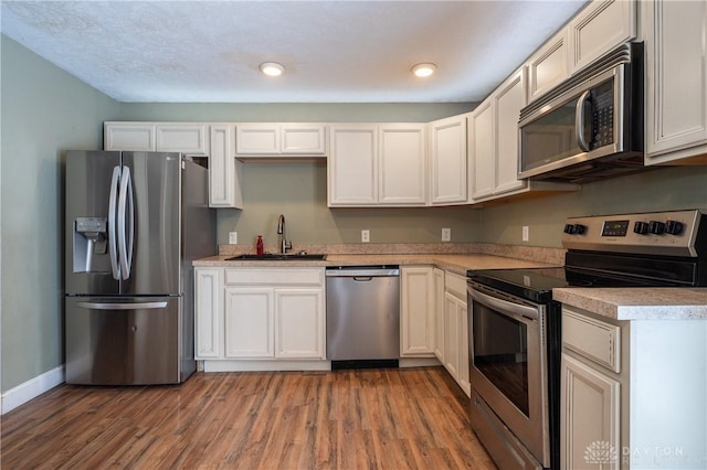 kitchen with light countertops, light wood-type flooring, baseboards, a sink, and appliances with stainless steel finishes