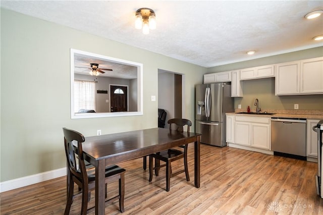 dining room featuring baseboards, light wood-style floors, ceiling fan, and a textured ceiling